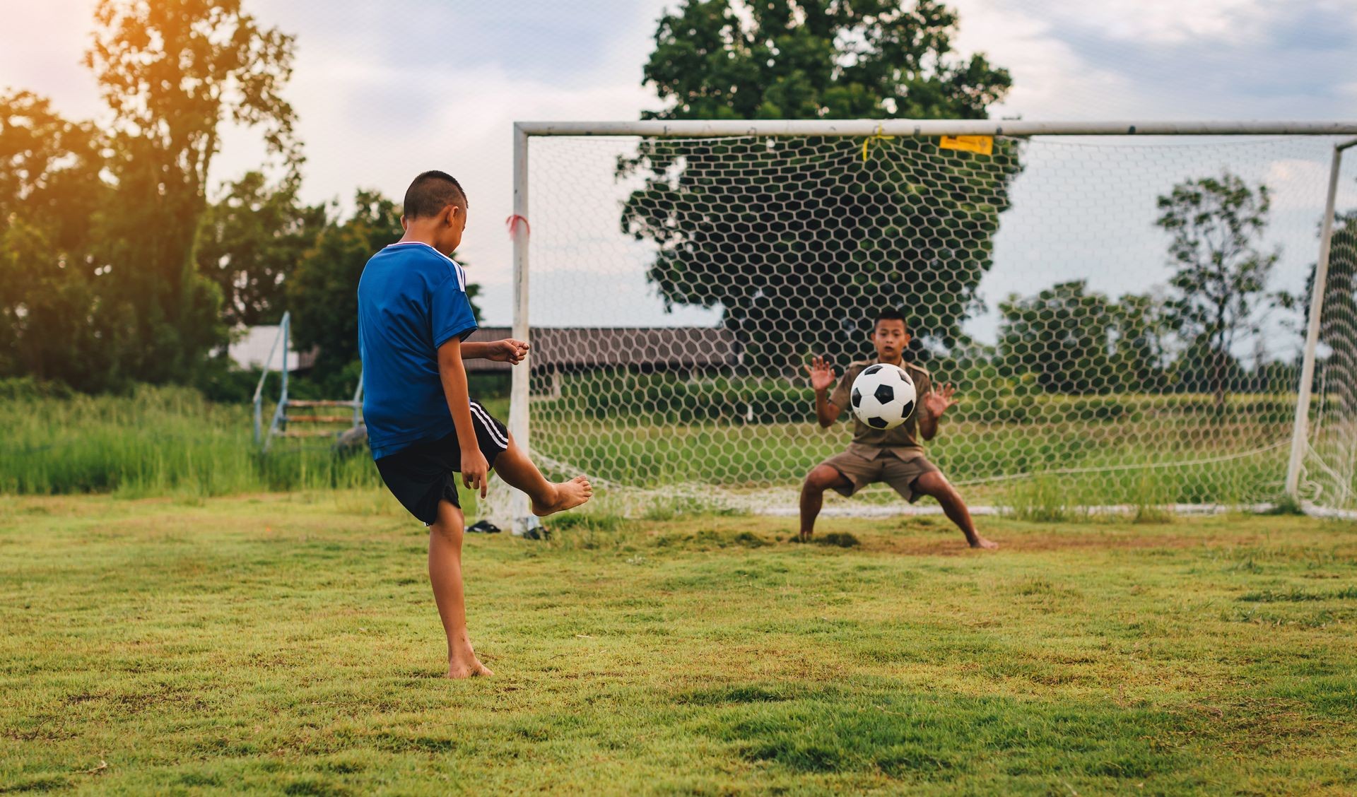 An action sport picture of a group of kid playing soccer football for exercise in community rural area under the sunset. 